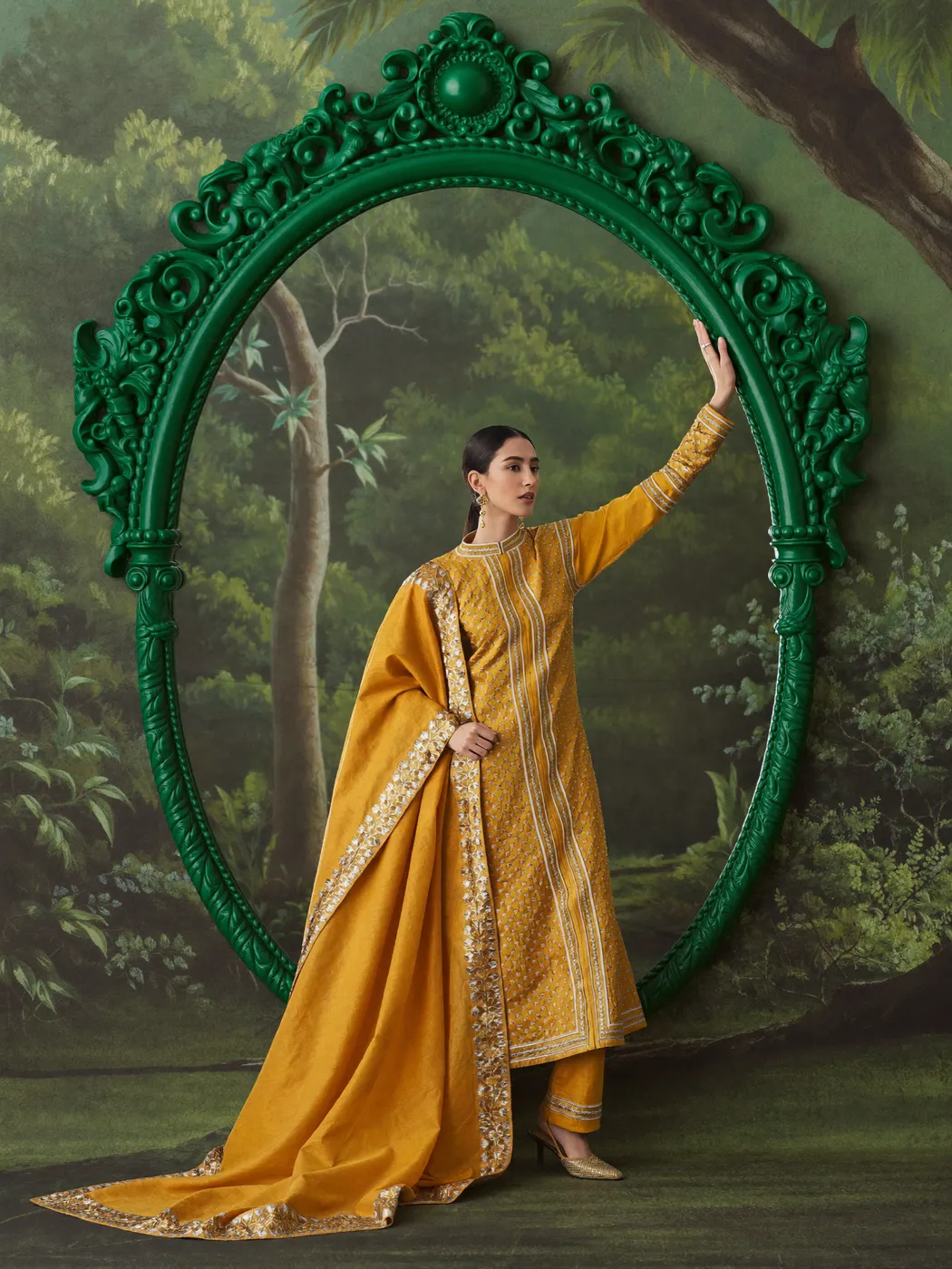 A woman in a mustard-gold embroidered kameez inside an emerald mirror frame