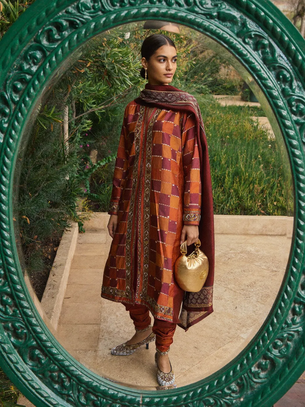 A woman in a rust block-printed shalwar kameez holding a gold potli